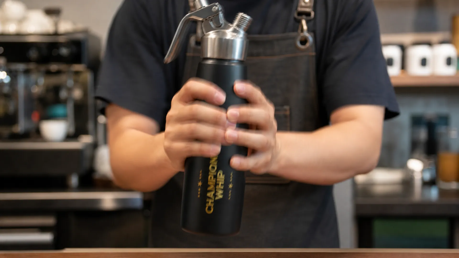 Shaking a stainless steel whipped cream dispenser vertically to reactivate residual N2O gas before dispensing upside down