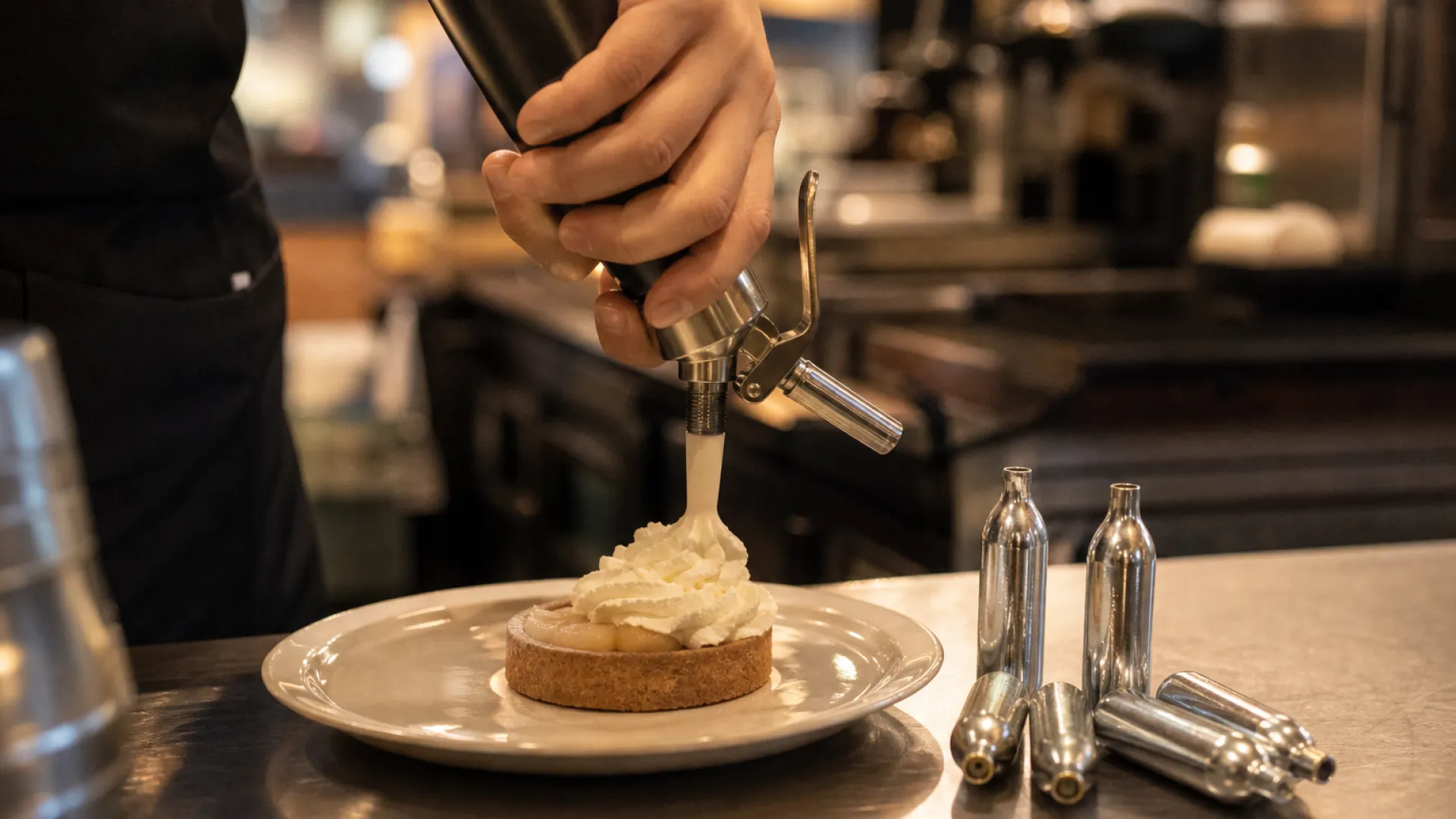 What are cream chargers used for: a stainless steel cream whipper dispensing fresh whipped cream over desserts in a café kitchen